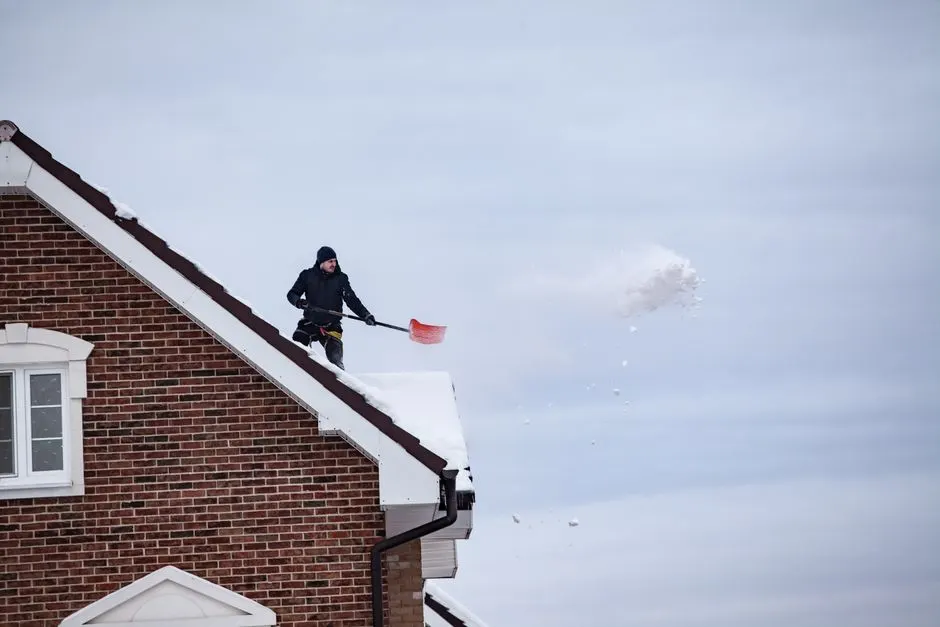A man shoveling snow off a rooftop, indicating winter outdoor activity.